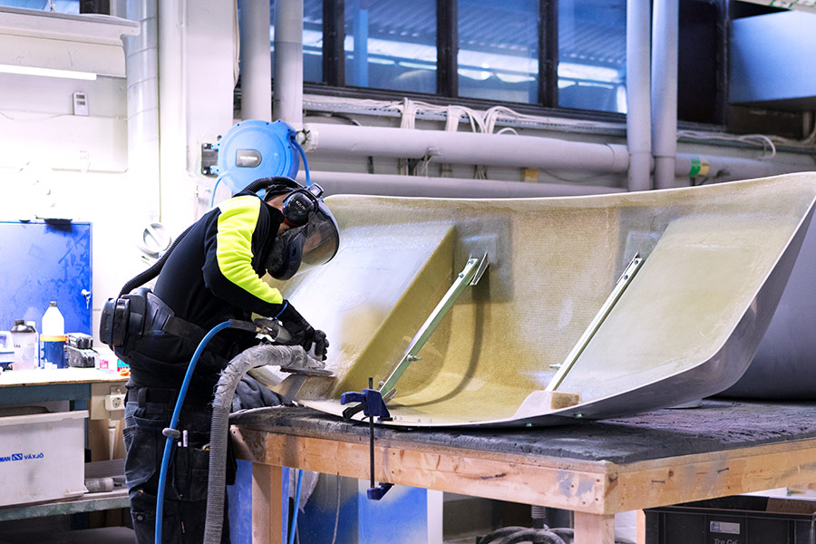 Medarbetare som slipar en stor detalj i glasfiberarmerad plast i verkstaden